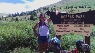 Alexandera Houchin with her arm over the sign denoting the Boreas Pass in Colorado during the Tour Divide