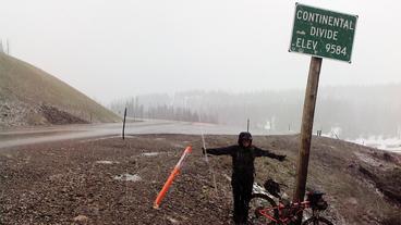 Alexandera Houchin's arms outstretched as she stand underneath a Continental Divide sign on the Togwotee Pass in Wyoming during the Tour Divide